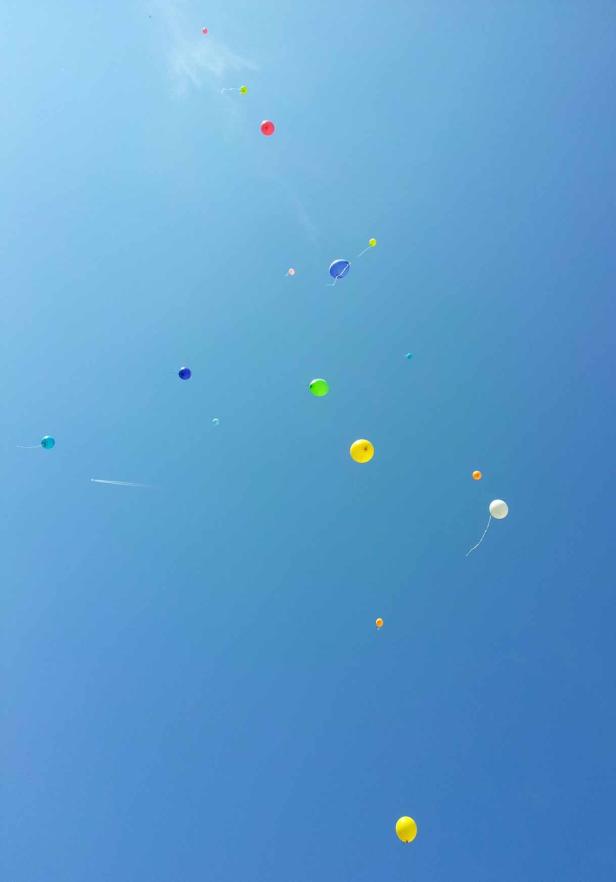 Viele bunte Ballons steigen in den blauen Himmel auf.