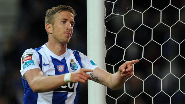 Ein Fußballspieler in einem blau-weißen Trikot zeigt auf das Tornetz.