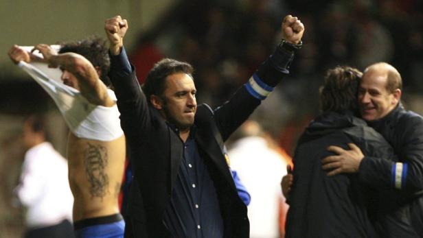 Ein Fußballtrainer und ein Spieler jubeln mit erhobenen Armen über einen Sieg.