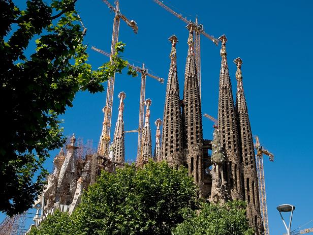 Die Sagrada Familia in Barcelona mit Baukränen vor blauem Himmel.