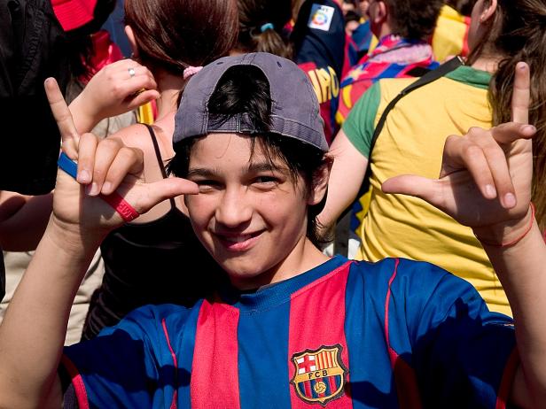 Ein lächelnder Junge im Barcelona-Trikot macht Handzeichen vor einer Menschenmenge.
