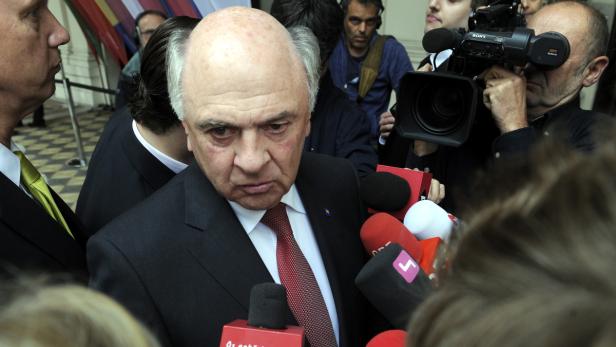 Ein Mann im Anzug steht vor einer Gruppe von Mikrofonen und Kameras.