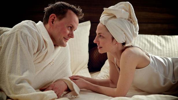 Ein Paar entspannt im Bett, die Frau mit einem Handtuch auf dem Kopf.