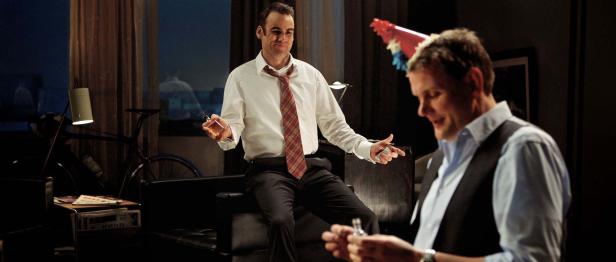 Zwei Männer in einem Wohnzimmer scheinen eine Art Geschäft abzuschließen.