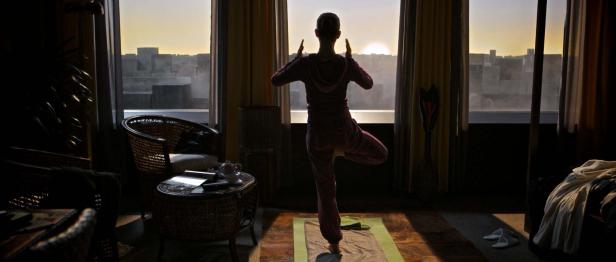 Eine Frau macht Yoga vor einem Fenster mit Blick auf eine Stadt bei Sonnenaufgang.