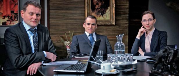 Drei Personen sitzen an einem Konferenztisch mit Laptops und Getränken.