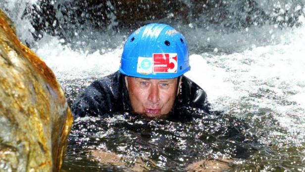 Ein Mann mit blauem Helm watet durch einen reißenden Fluss.