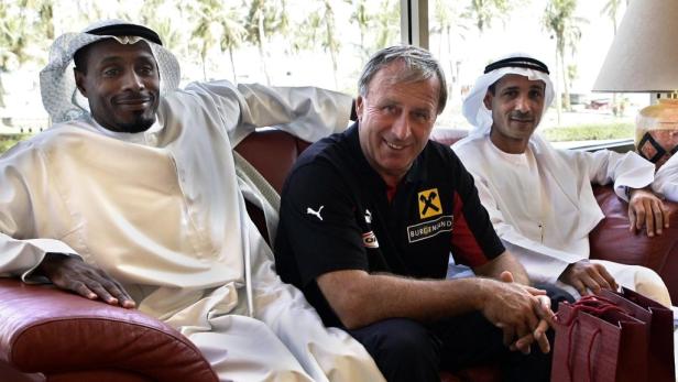 Drei Männer sitzen auf einem roten Sofa, zwei davon in traditioneller arabischer Kleidung.