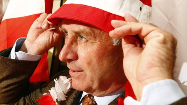 Ein Mann setzt einen rot-weißen Hut auf, möglicherweise bei einer Sportveranstaltung.