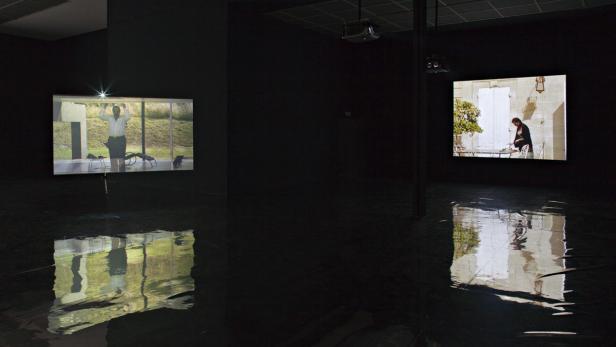 Eine Kunstausstellung mit zwei Videoprojektionen, die sich im Boden spiegeln.