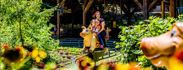 Eine Frau mit zwei kleinen Mädchen fährt auf einer Schweinchenbahn durch einen Freizeitpark.