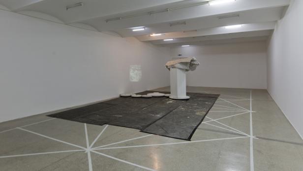 In einem Ausstellungsraum steht eine Skulptur auf einem weißen Sockel.