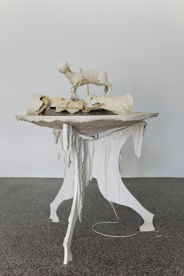 Eine weiße Skulptur eines Lamms steht auf einem ungewöhnlichen, zerklüfteten Tisch.