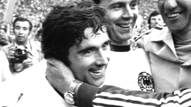 Ein lächelnder Fußballspieler wird von seinen Teamkollegen umarmt.