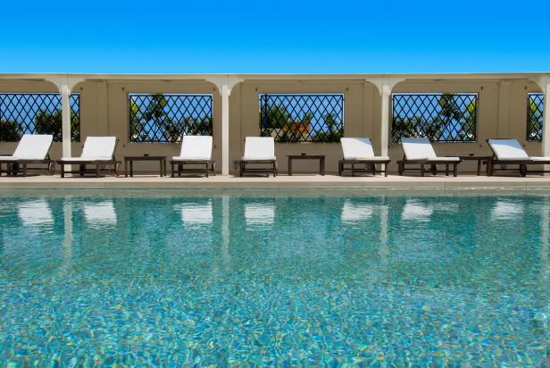 Mehrere Liegestühle stehen am Rande eines türkisfarbenen Pools.