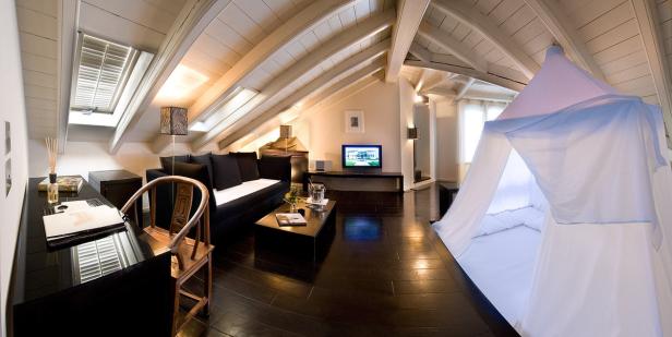 Ein Zimmer mit Dachschrägen, dunklem Holzboden, einem Himmelbett und einem Schreibtisch.