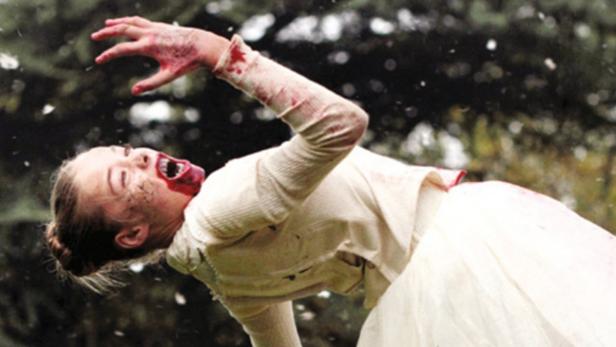 Eine verletzte Frau in einem weißen Kleid schreit mit blutverschmiertem Gesicht.