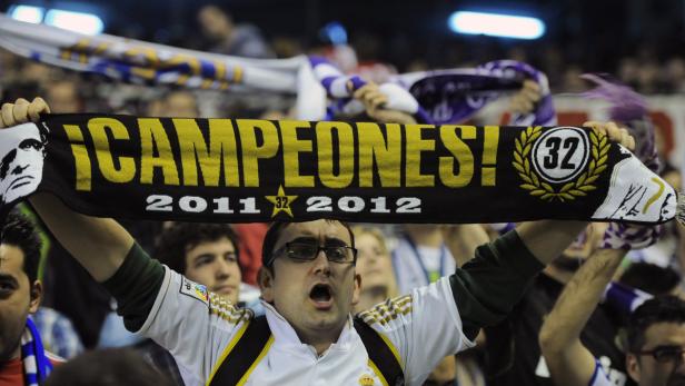 Ein Mann hält einen Schal mit der Aufschrift „¡Campeones!“ und den Jahreszahlen 2011 und 2012 hoch.