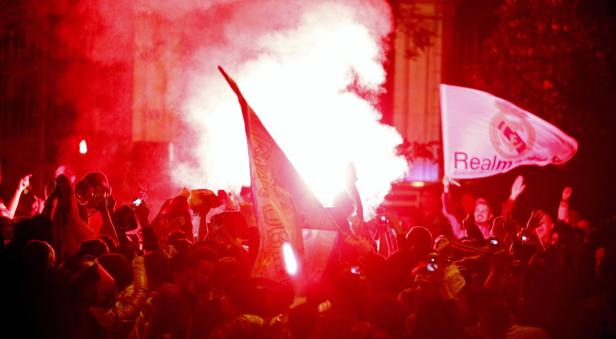 Eine Menschenmenge feiert mit Fahnen und roter Pyrotechnik.