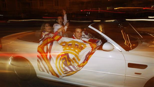 Junge Leute feiern in einem weißen Cabrio mit einer Real Madrid Flagge.