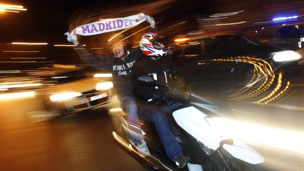 Zwei Männer fahren auf einem Motorroller, einer schwenkt einen „Madrid C.F.“-Schal.