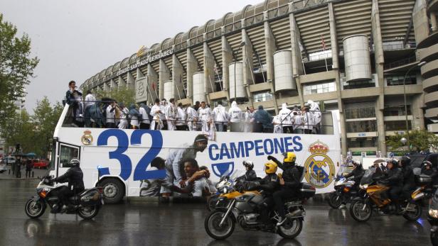 Ein Bus mit Real Madrid-Spielern fährt unter Polizeieskorte durch die Stadt, im Hintergrund das Estadio Santiago Bernabéu.