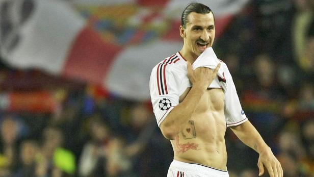 Zlatan Ibrahimović mit freiem Oberkörper und Tattoos auf dem Bauch, in einem Fußballstadion.