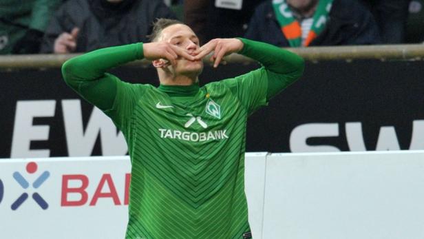 Ein Fußballspieler im grünen Trikot von Werder Bremen jubelt mit den Händen am Mund.