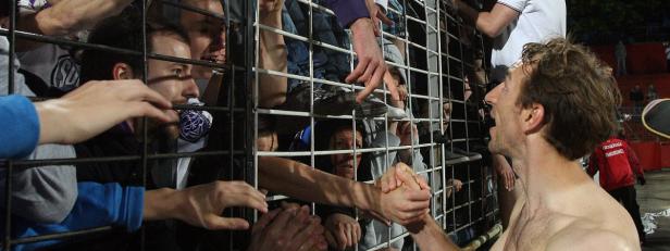 Ein barfüßiger Fußballspieler gibt Fans hinter einem Zaun die Hand.