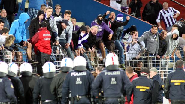 Polizisten stehen vor einer Gruppe Fußballfans hinter einem Zaun.