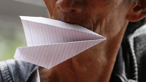 Ein Mann hat ein Papierflugzeug im Mund.
