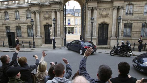 Menschen winken einer Fahrzeugkolonne vor dem Élysée-Palast in Paris zu.