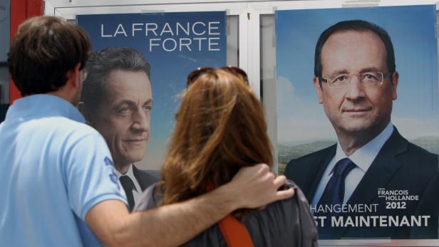Ein Paar betrachtet Wahlplakate von Nicolas Sarkozy und François Hollande.