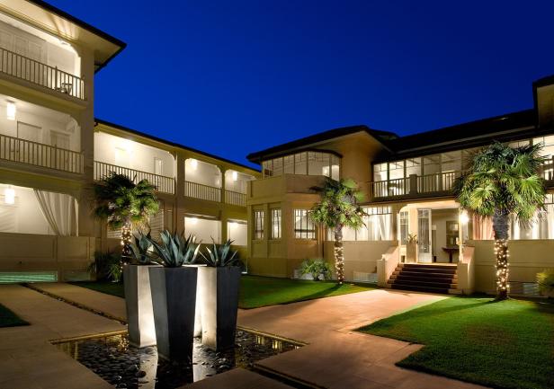 Ein beleuchtetes Hotel mit Palmen und einem kleinen Wasserbecken in der Nacht.