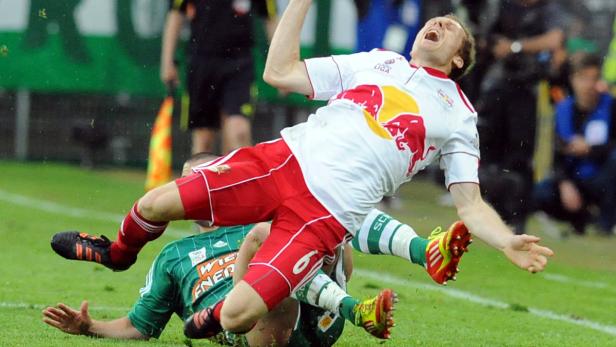 Ein Fußballspieler in einem roten Trikot wird gefoult und schreit.