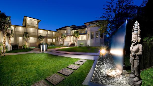 Ein großes, beleuchtetes Gebäude mit Rasenfläche, einem Wasserfall und einer Statue im Vordergrund.