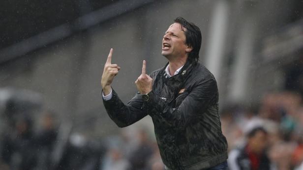 Ein Mann in einer schwarzen Jacke gestikuliert mit erhobenen Zeigefingern im Regen.