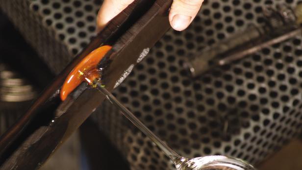 Ein Glasbläser formt eine orangefarbene Glasmasse mit Werkzeugen.