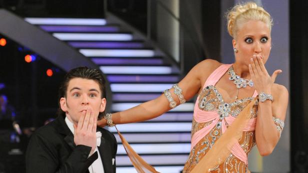 Ein Mann im Smoking und eine Frau im Ballkleid halten überrascht die Hände vor den Mund.