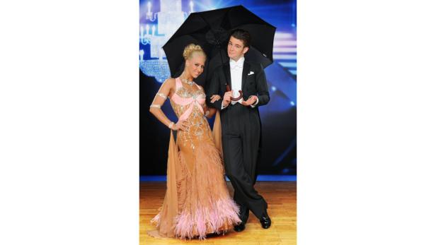 Ein Mann im Smoking hält einen Regenschirm über eine Frau im Ballkleid.