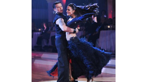 Ein Tanzpaar führt eine leidenschaftliche Rumba auf einer Bühne auf.