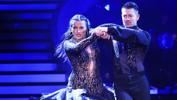 Ein Tanzpaar in glitzernden Kostümen tanzt auf einer Bühne mit blauem Licht.