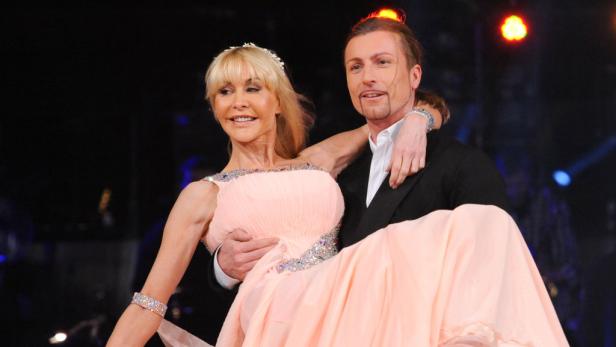 Ein Mann im Anzug trägt eine Frau im rosa Ballkleid.