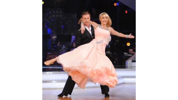 Ein Tanzpaar führt eine elegante Drehung auf einer Bühne auf.