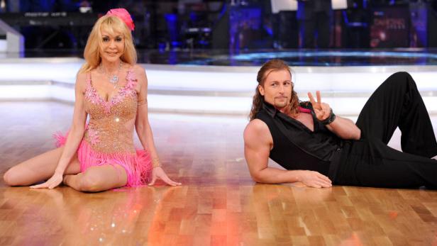 Eine Frau in einem rosa Tanzkleid und ein Mann liegen auf einem Parkettboden.