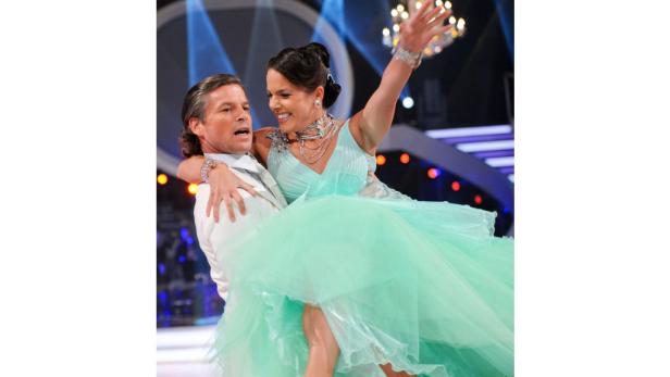 Ein Mann im weißen Anzug trägt eine Frau im mintgrünen Ballkleid.