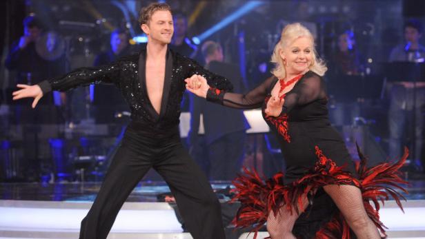 Ein Mann und eine Frau tanzen in glitzernden Kostümen auf einer Bühne.