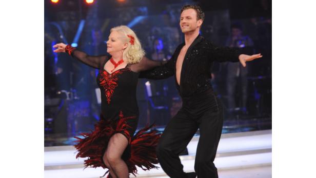 Ein Tanzpaar in schwarzen, rot verzierten Kostümen auf einer Bühne.