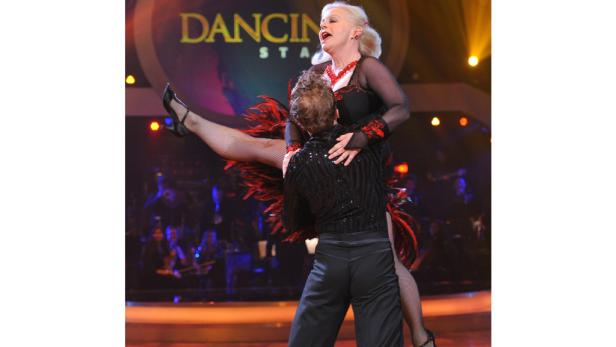 Ein Tanzpaar führt eine Hebefigur auf einer Bühne auf.