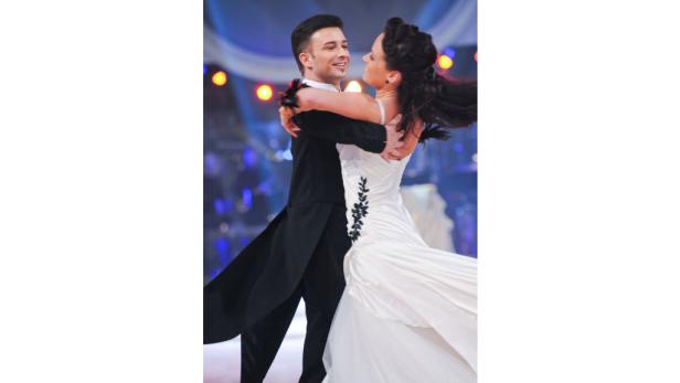 Ein Tanzpaar in festlicher Kleidung umarmt sich auf einer Bühne.